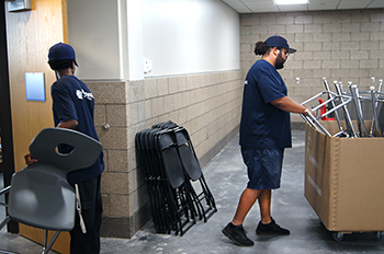 Two movers replace folding chairs with new chairs.