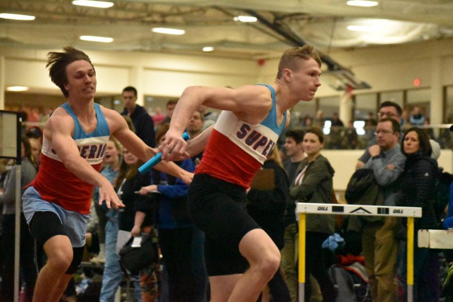 Junior Noah Benson hands off the baton to junior Brady Herbst during the 4x200-meter relay. The boys’ team took third and the girls’ team took fifth at the annual Packy Paquette Invitational track meet Friday night.