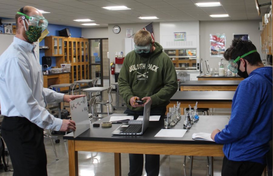 Tyler Ross explains an equation to an online student at the lab station in room 1150 while Trevor Bickford and Cameron Buck start the experiment May 4.