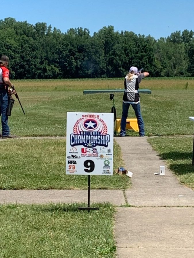 Junior Abby Peterson, and Alumni Justin Kimmes and Ethan Peterson standing in front of the National Clay Target League Championship banner on July 9-16, 2022 at Cardinal Shooting Centre, Marengo, Ohio.