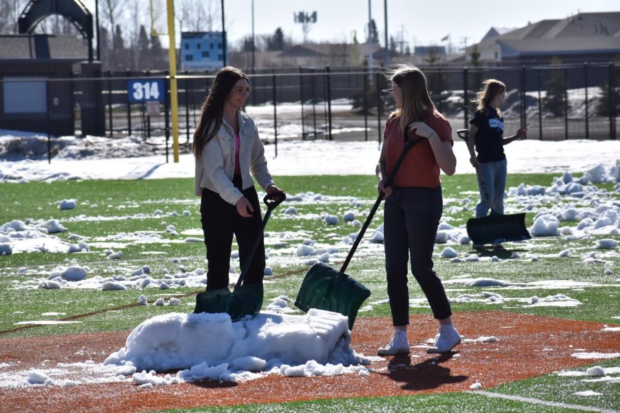 Sophomore Ava Stratton talks with a fellow student while they shovel the leftover snow off the baseball field in the NBC Spartan Sports Complex on Tuesday, April 11, 2023, in preparation for the 2023 Spring Sports Season.