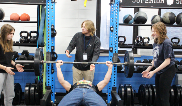  Junior Paige Johnson (left) and Junior Kaitlyn Forester (right) being instructed on how to spot Senior Sam Hoff by new Strength and Conditioning teacher Gunner Johnson on November 27, 2023.
