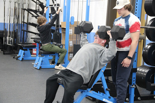 Haydon Stallsmith (center) presses 80 pound dumbbells working out in his Strength and Conditioning class on May 15, 2024. Stallsmith is spotted by Cody Pahos (right) so he doesnt hurt himself during the lift.