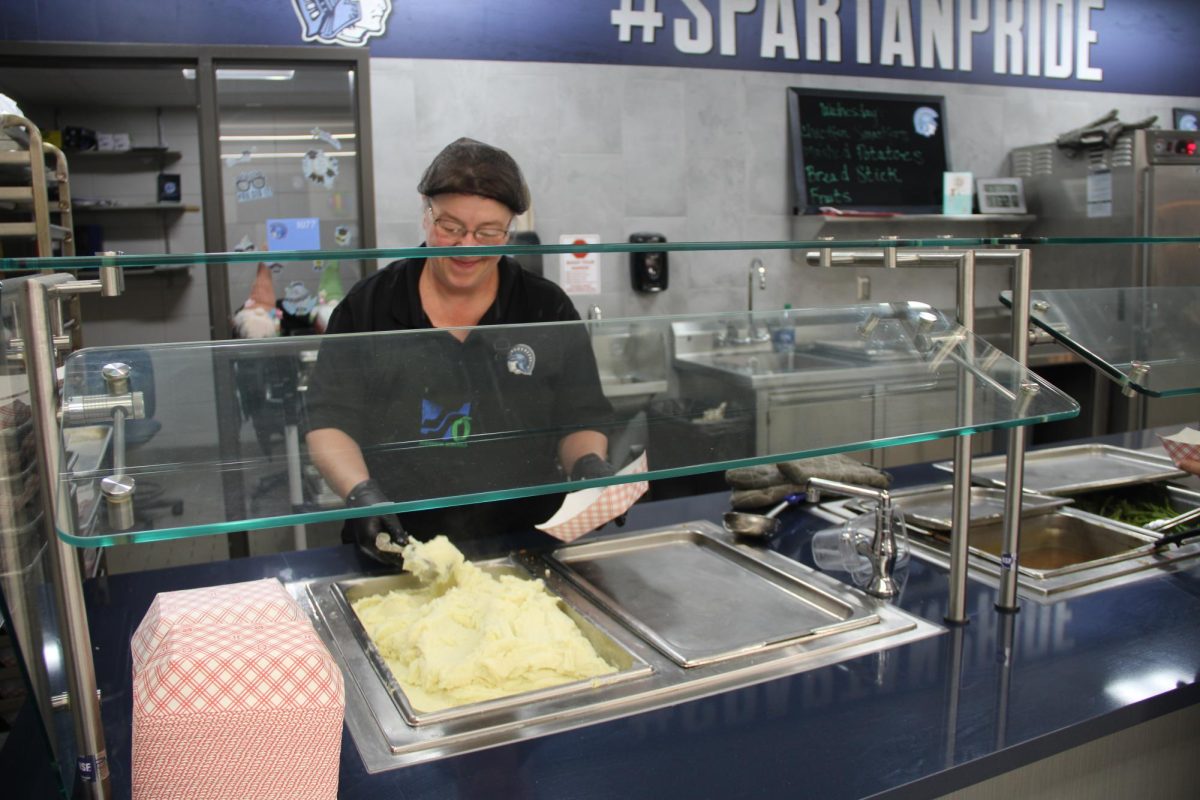 Lunch worker Mel Young scoops creamy mashed potatoes into a paper boat during B lunch on May 29, 2024. 