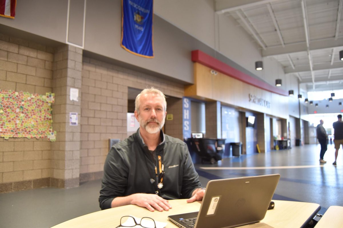 Dean Bryan Denninger poses while sitting at a lunch table in the commons on May 3, 2024. Denninger’s job is hands-on and busy, so he doesnt always have time to sit at his desk and usually makes a lunch table his workspace. 
