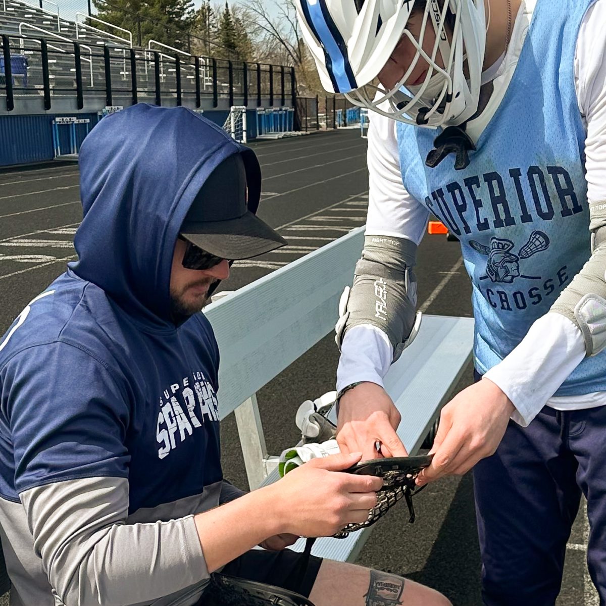 Coach Travis Herrboldt (left) helps fix sophomore Maverick Warring lacrosse head on the bench of the NBC Sports Complex on May 6, 2024. Herrboldt has a unique relationship with his players.