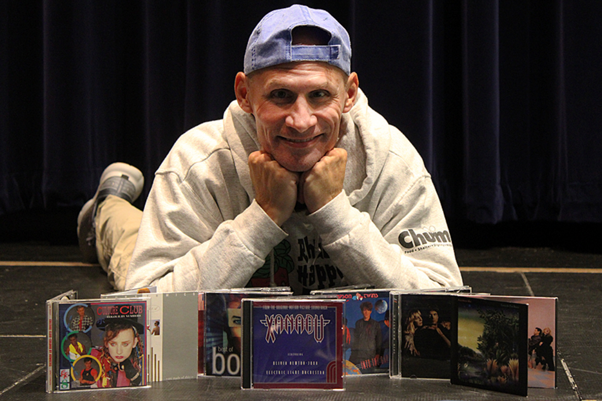 Instructional coach and co-director Andy Wolfe poses on the stage in the Performing Arts Center with CDs dating back to the 1980s on Sept. 28, 2024. The music is Wolfe's inspiration  A Midsummer Night's dream with “Xanadu” by Electric Light Orchestra and Olivia Newton-John being front and center.