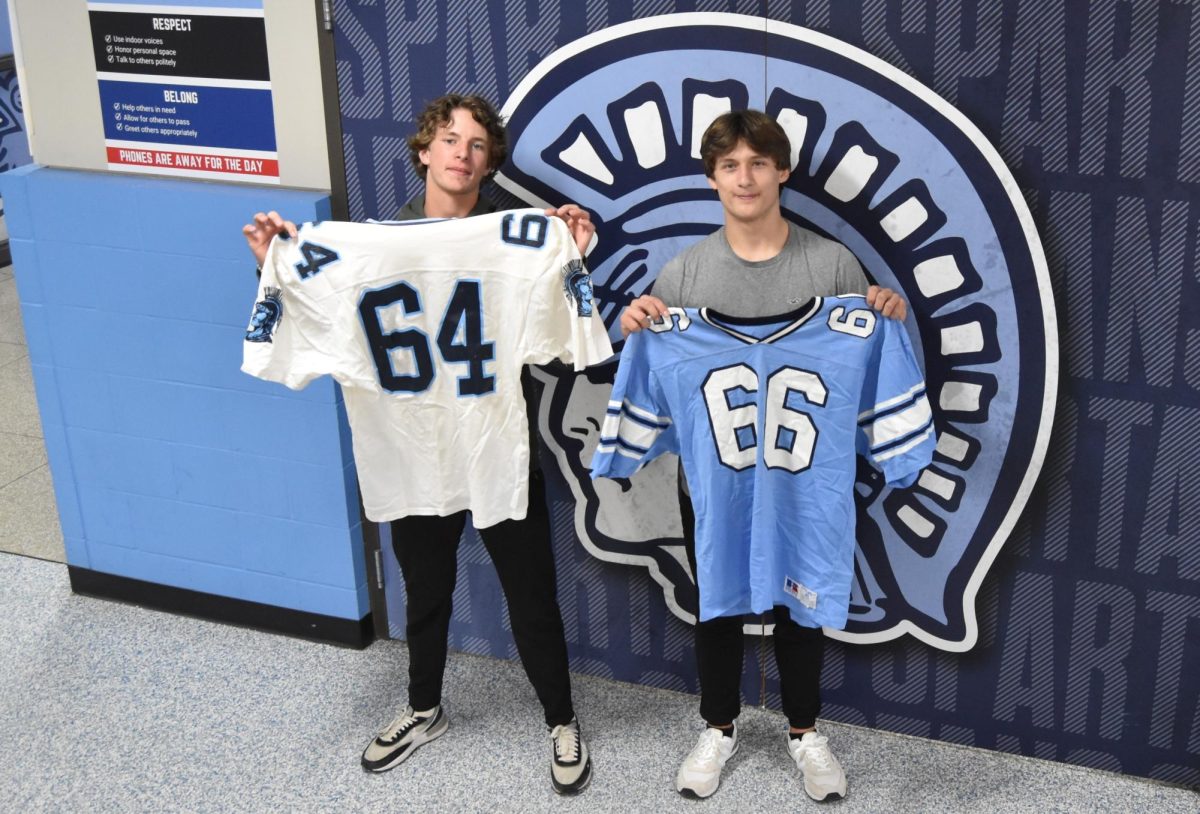 Juniors Sam Hubbard (left) and Brady Haroldson (right) hold up vintage football jerseys outside of the wrestling room on Tuesday, Oct 1. These old jerseys are being sold in the Spartan Shack for $20 each.