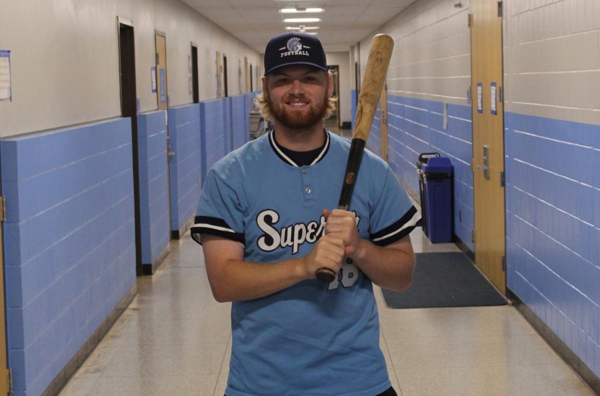 Gym teacher Gunner Johnson stands in the locker room hallway with his old Superior baseball jersey on while he holds a baseball bat on Sept. 20.