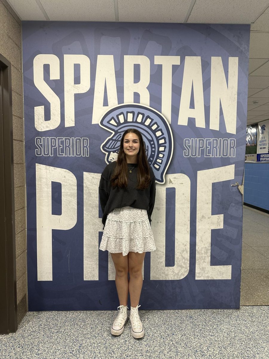 Sophomore Isabelle Barker poses in front of the spartan pride wall. Barker sings the national anthem before volleyball games.