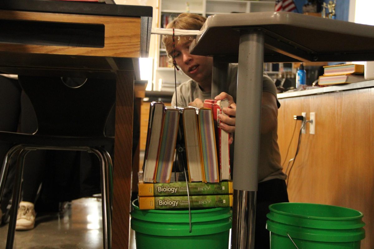  Junior Matthew Youngberg places textbooks on top of a bucket filled with water in order to break a handmade bone on Feb. 6, 2025. During second and sixth hour Human Anatomy and Physiology students in science teacher Lee Sims class were instructed to break their handmade bones to see how much weight it would take to snap.
