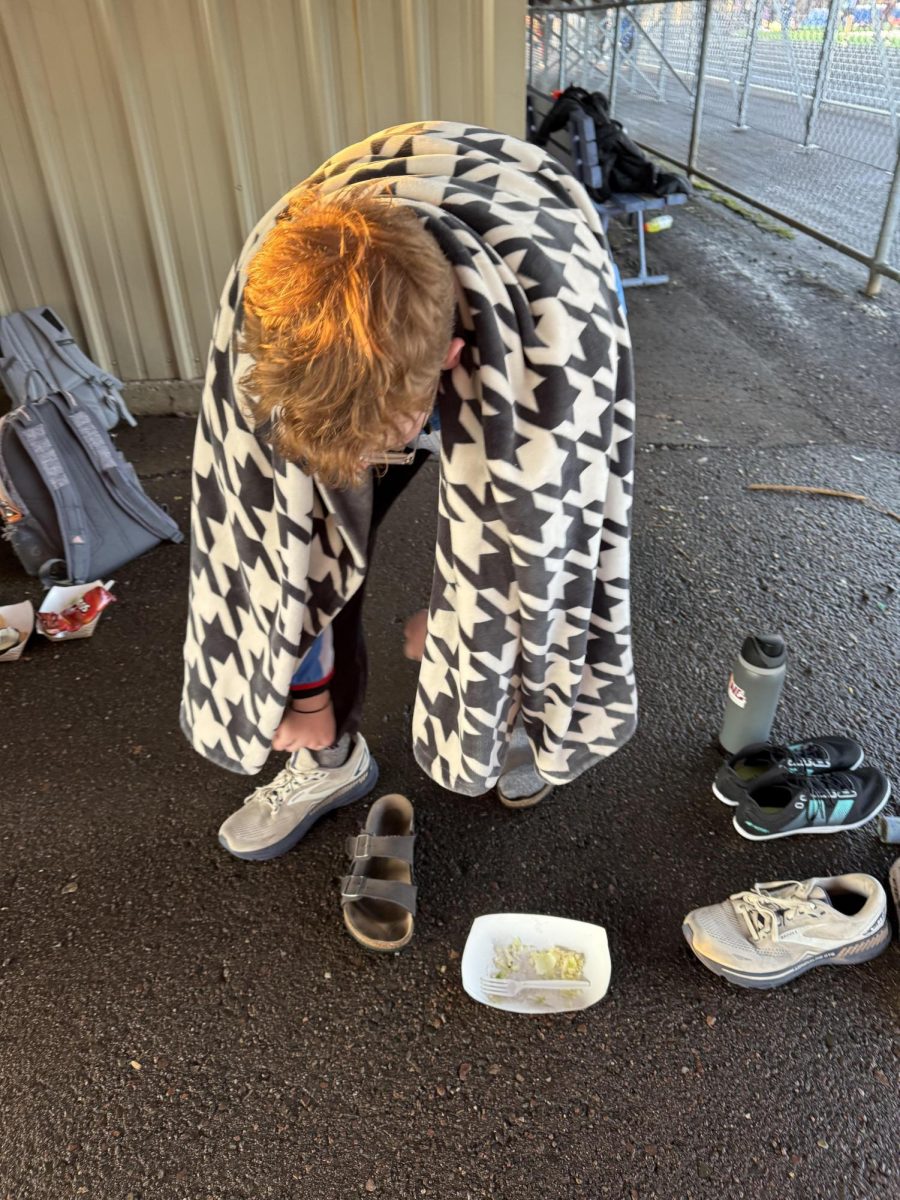 Senior distance captain Nolan Bird unwinds after running the mile at Cloquet track meet on April 22.  Following his race, Bird secured in his warm blanket to support the rest of his team on the cold meet day. 