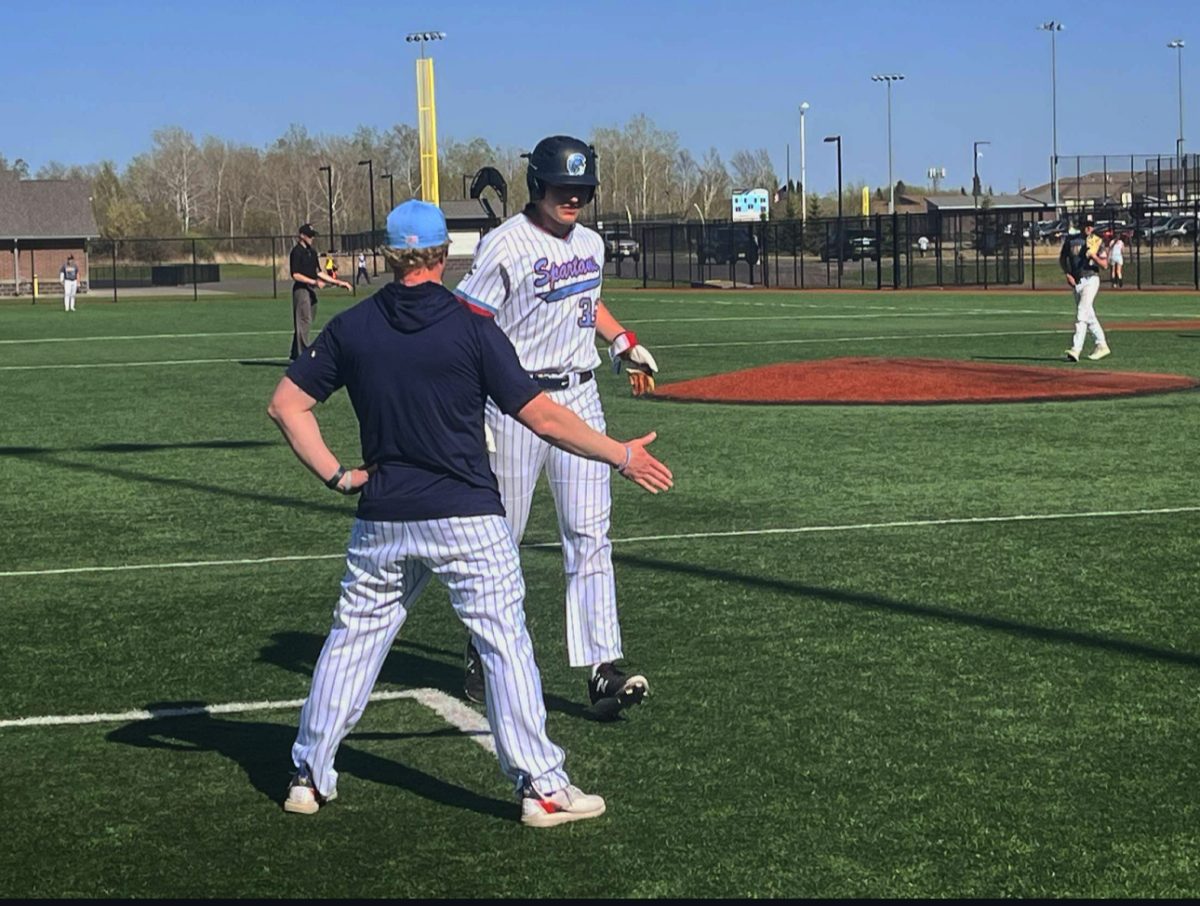 Senior outfielder Hudsen Helenius high fives coach Ryan Hendry after coming off the bases during their game against Hermantown on May 3, 2025. Helenius is a power hitter for the Spartans this year hitting third in the lineup. 
