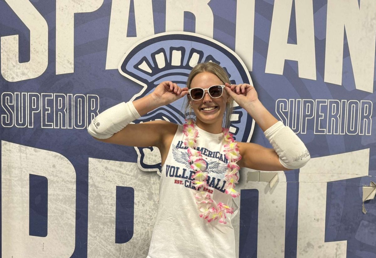 Junior Claire Egnash poses with summer accessories and volleyball attire in front of the Spartan wall on April 24. 