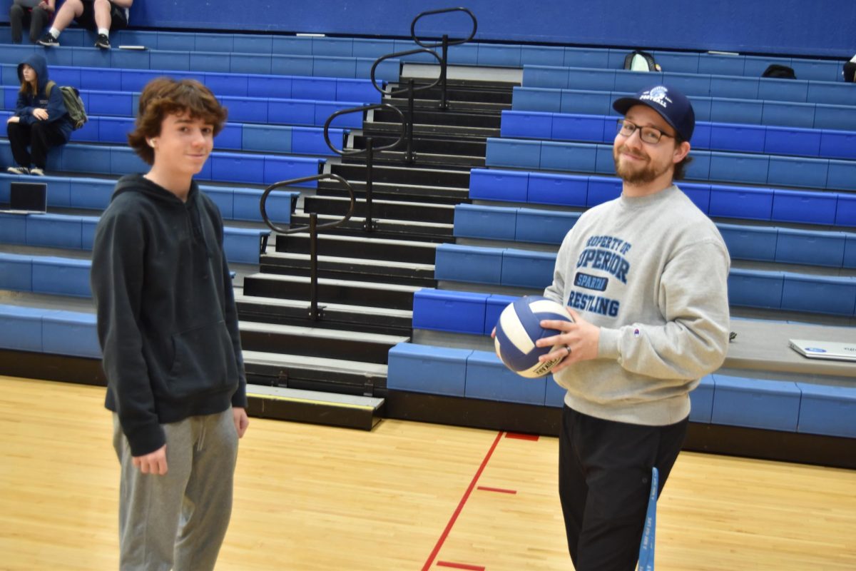 Coach Long talks with student about how to serve in volleyball in 7th hour gym class. 