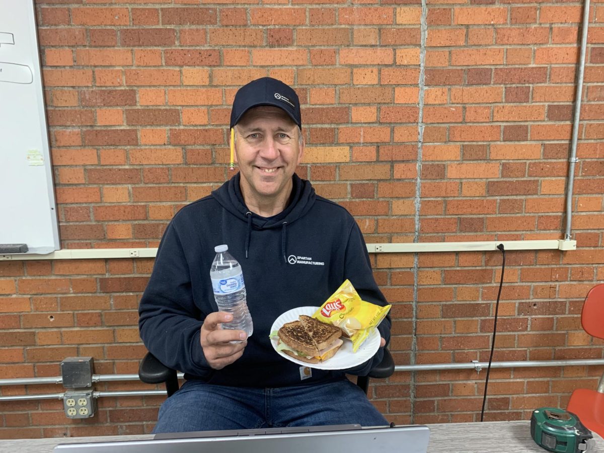 Industrial tech teacher Pete James enjoys a sandwich, chips and water delivered by junior Beckett Selden on May 15, 2025. The meal was prepared as part of an essentinal unit that showcases the student's culinary skills in foods two.