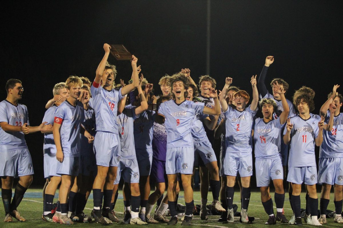 Senior captain Peyton Franta (10) jumps up as he holds the conference championship plaque while the rest of the Spartans jump around him on the field of the NBC Spartan Sports Complex on Oct. 6 2025. The Spartans held this event after their game against Rice Lake, their first game since beating Proctor to be named champions.