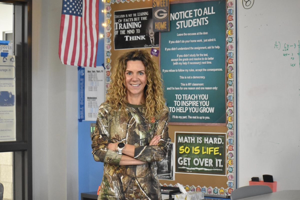Coach and math teacher Lindsey Smith poses in front of her math posters showing her school spirit by deciding to wear camouflage for the theme day. Smith demonstrates her school spirit while being a coach and a teacher. 