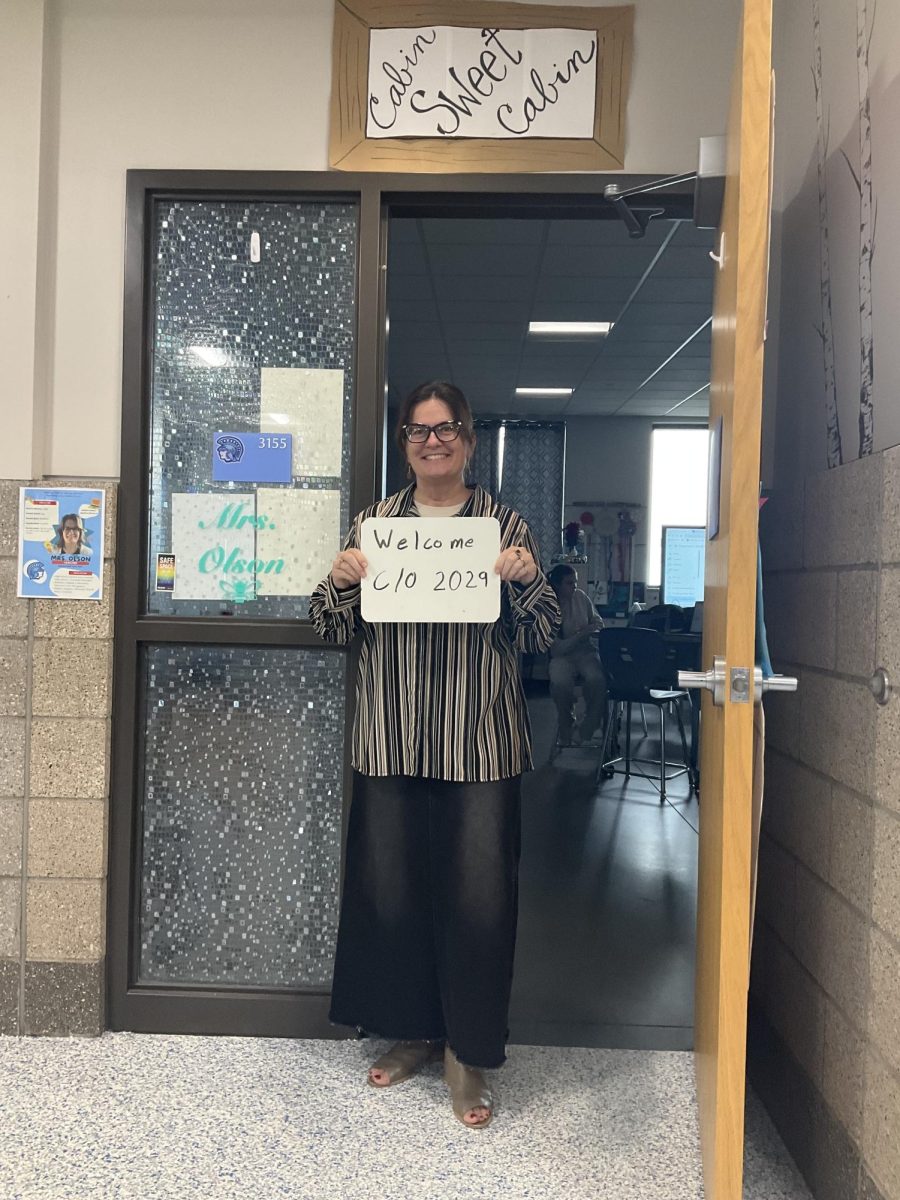 Veteran civics teacher Jaclynn Olson holds a whiteboard welcoming the class of 2029 outside of her classroom following homecoming week on September 30, 2025.