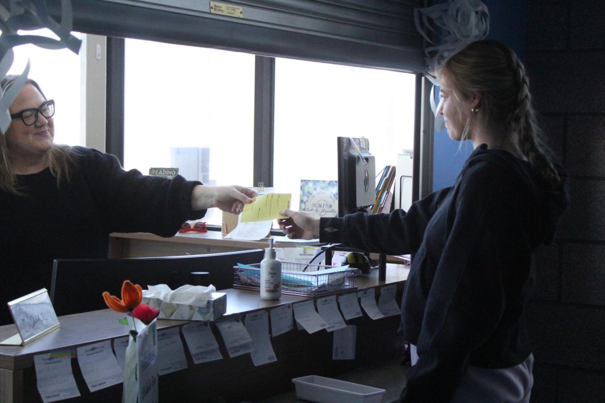 Attendance secretary Elaine Homberg hands a tardy pass to a late student on Feb. 25. 