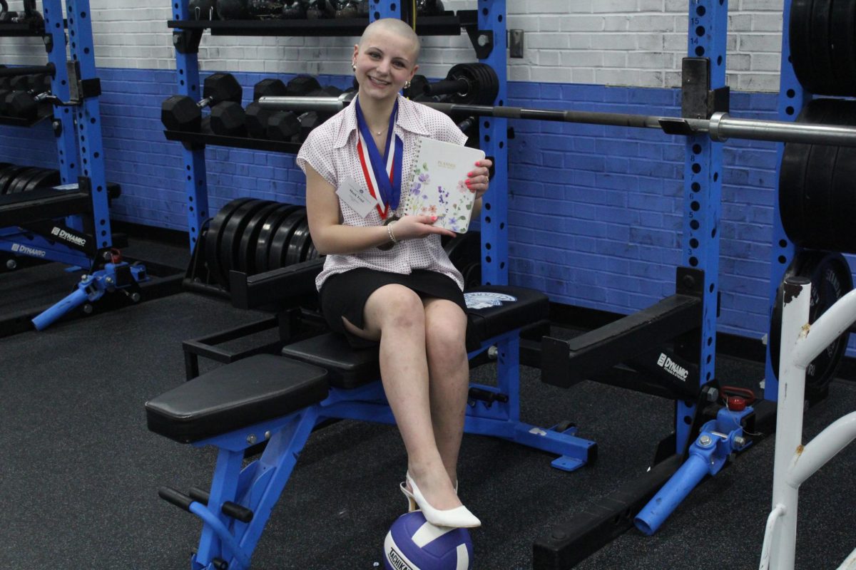 Sophomore Tylee Savoye sits on the bench in the Spartan Weight room with her mock trial outfit on, showing her planner right beside her and with her foot resting on a volleyball.