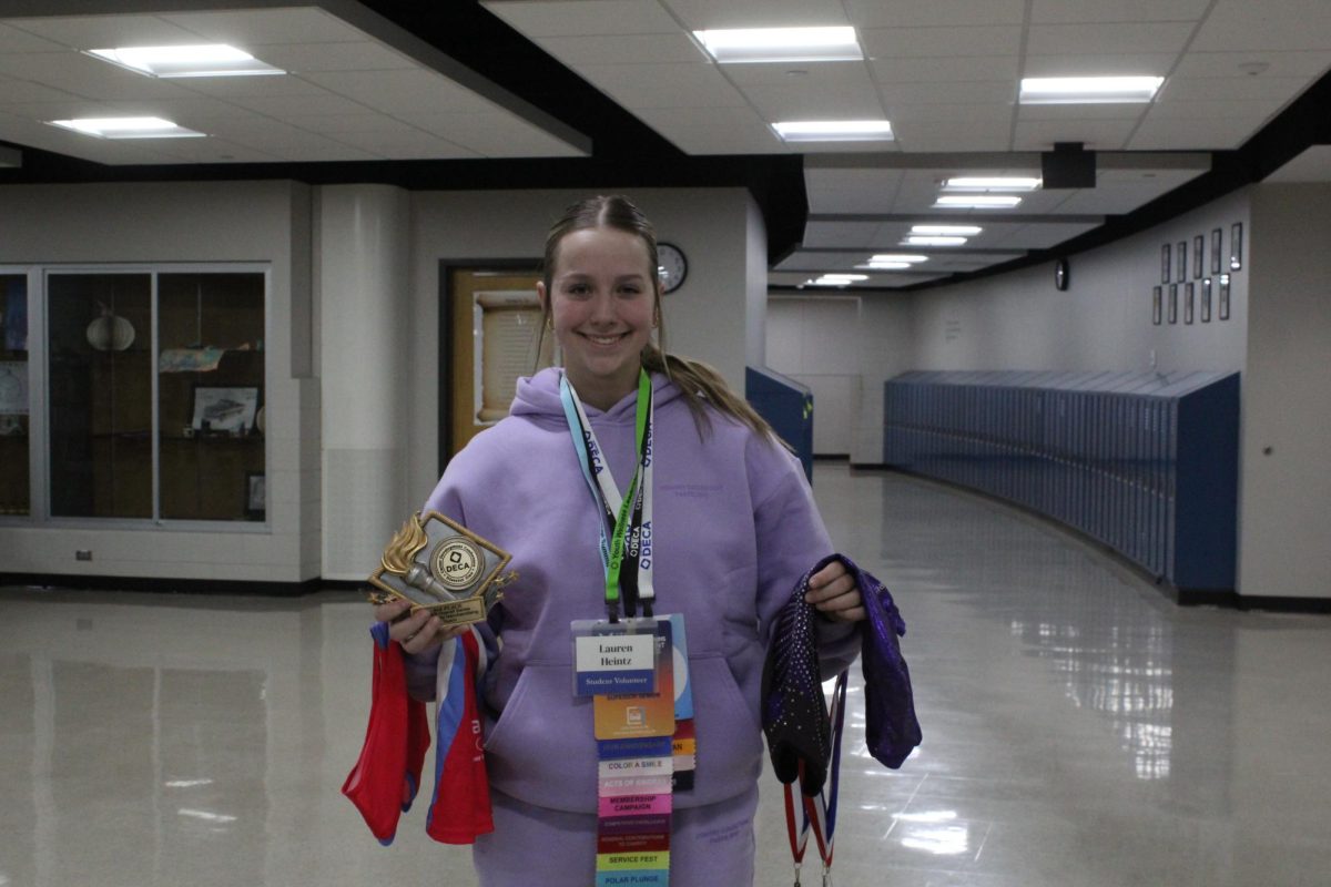 Lauren Heintz holding her gymnastic leotard, volleyball jersey, DECA trophy, and her DECA lanyards.