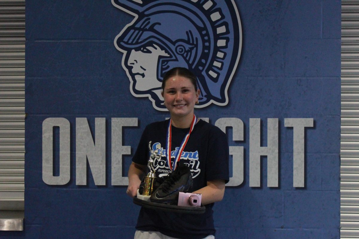Junior Lily Clark posing with her tennis racket, tennis trophy, and camera.