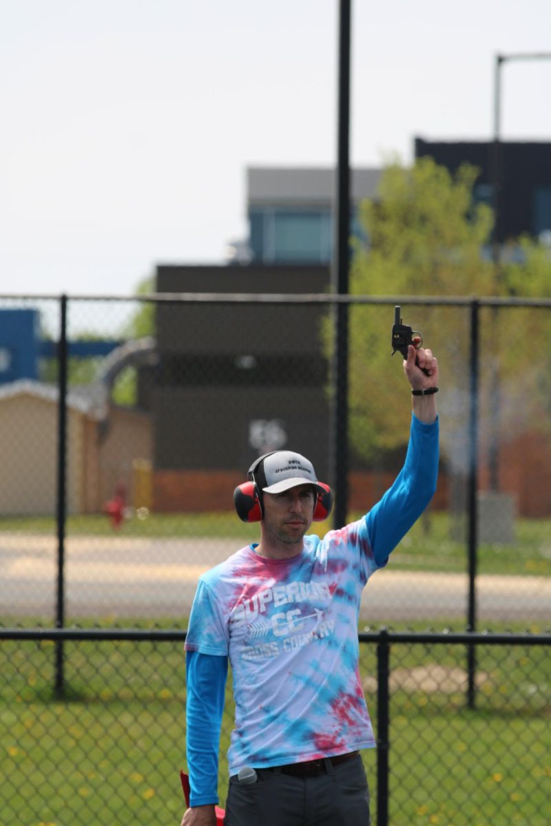 Science teacher and cross country coach Lee Sims holds up the starting gun to indicate the start of a race on June 1 at the NBC Spartan Sports Complex 

